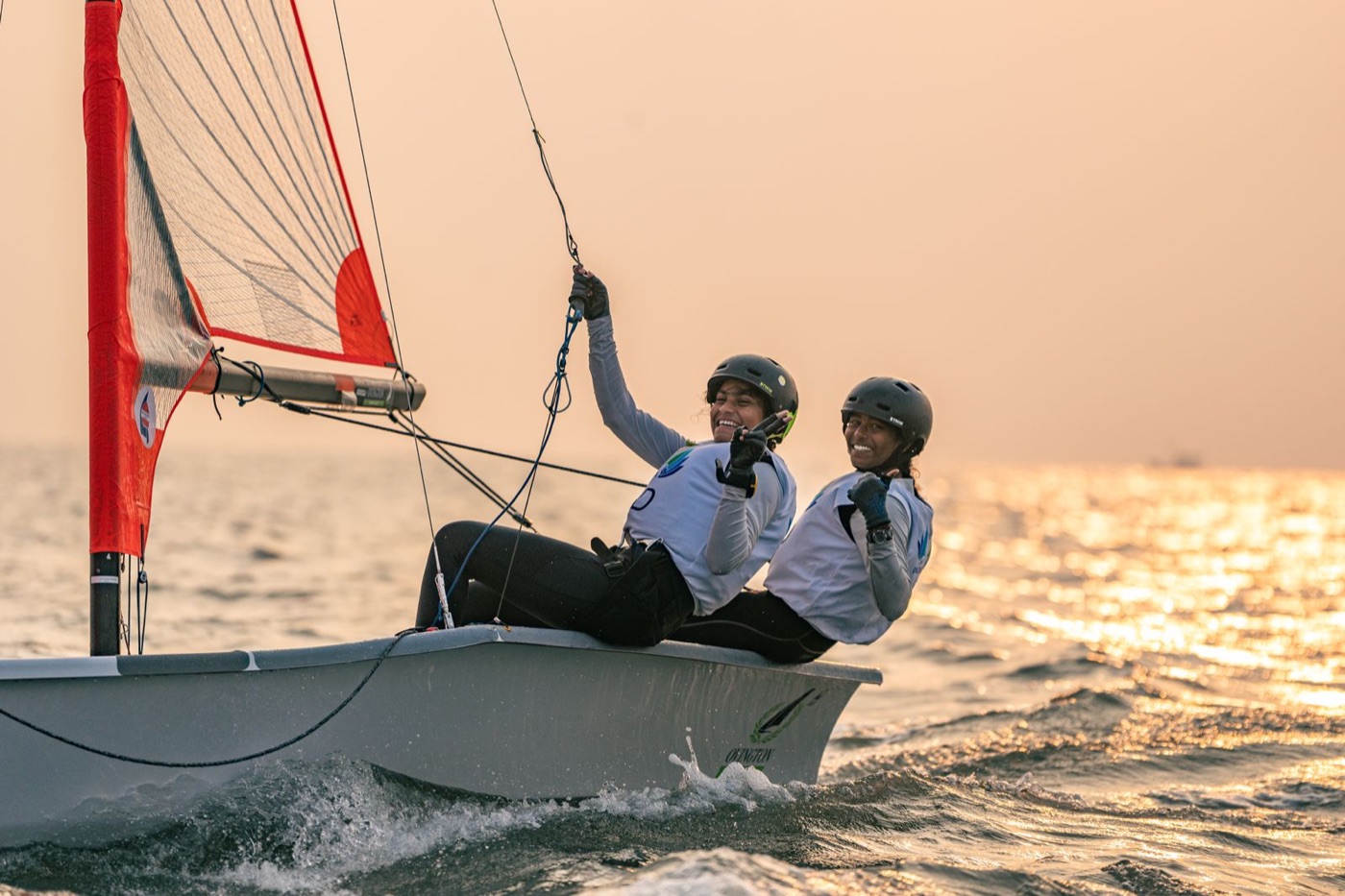 Two young sailors smiling aboard a dinghy on open water at golden hour, Hyderabad.