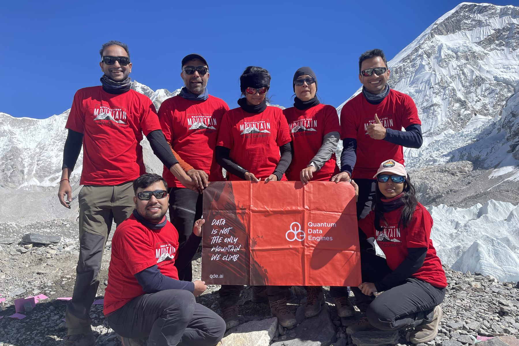 The QDE team in branded tees at Everest Base Camp, holding the company flag