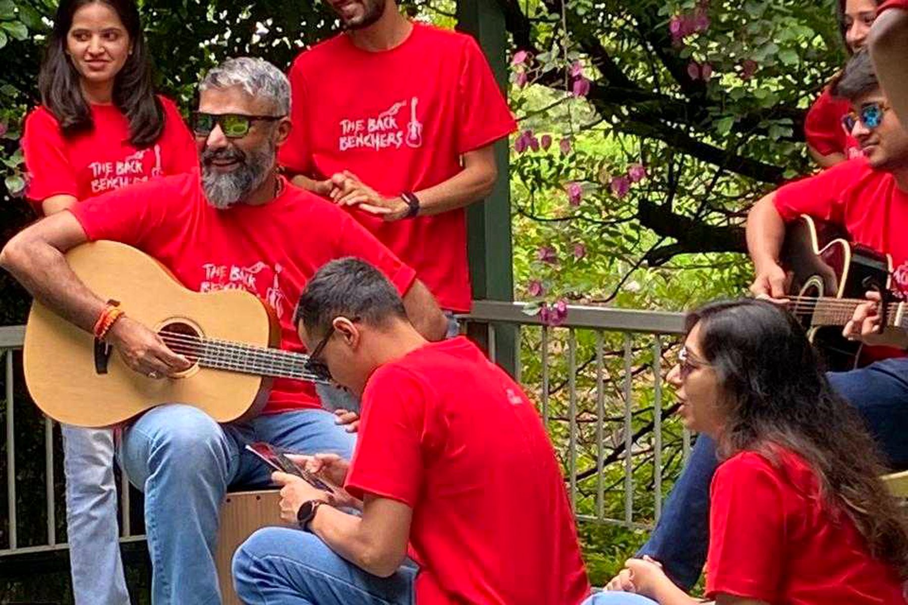 Band members in red tees playing guitar together among the flowers
