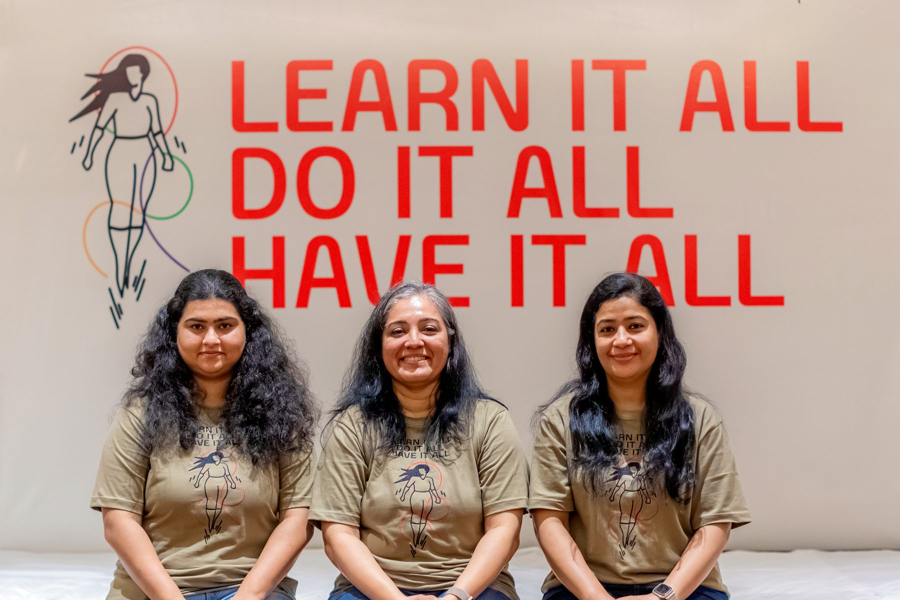 Three women in WEEW tees in front of the 'Learn it all, do it all, have it all' wall